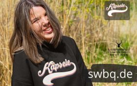 frau auf der wiese mit schwarzem hoodie mit kaepsele motiv