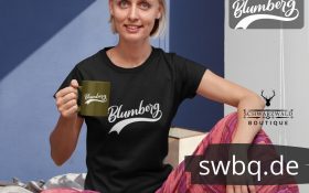 frau sitzend auf dem bett mit tasse und schwarzem t-shirt mit blumberg aufdruck