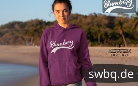frau am see mit lila hoodie mit blumberg aufschrift