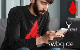 mann mit handy und schwarzem t-shirt mit rote schwarzwald tanne design