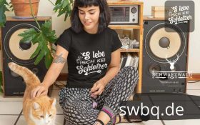 frau mit katze auf dem boden sitzend mit schwarzem tshirt mit motiv das leben ist kein schlotzer alemannischer spruch